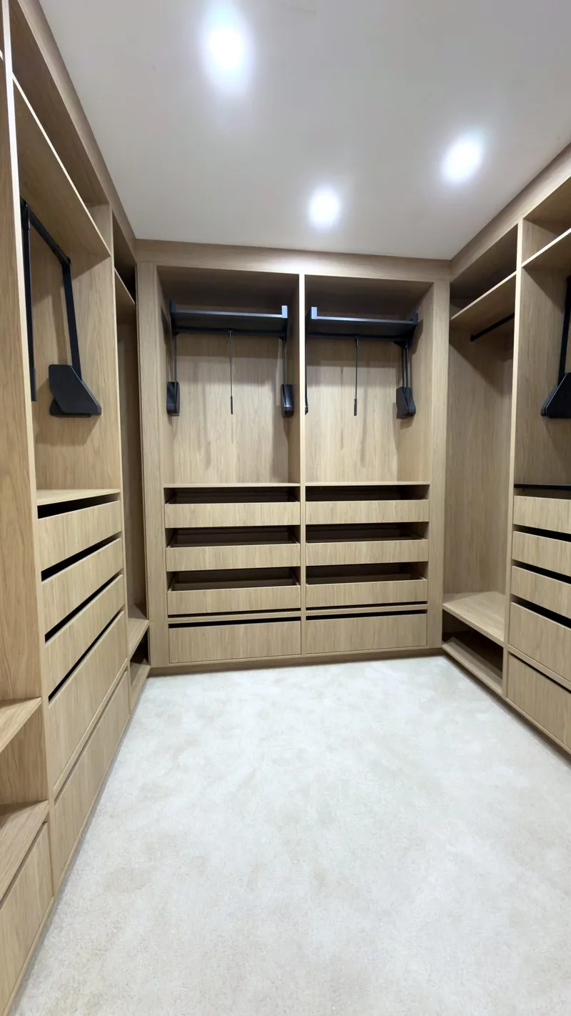 U-shaped oak walk-in wardrobe with pull-down hanging rails, drawer banks and downlights