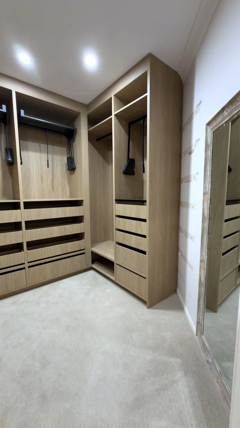 Corner view of an oak walk-in wardrobe with pull-down rails and drawers