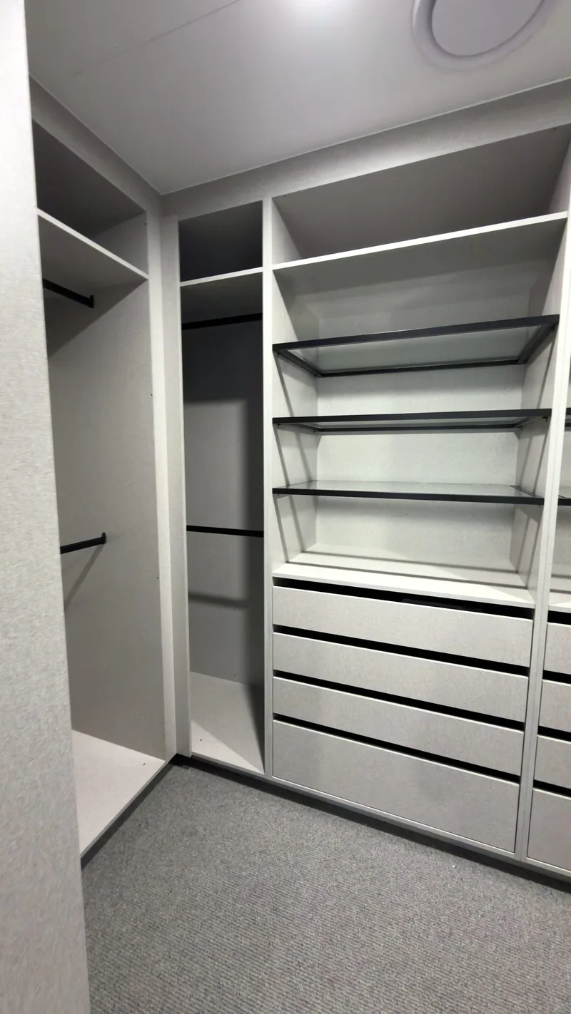 Angled view of a grey walk-in wardrobe with glass shelves and hanging space