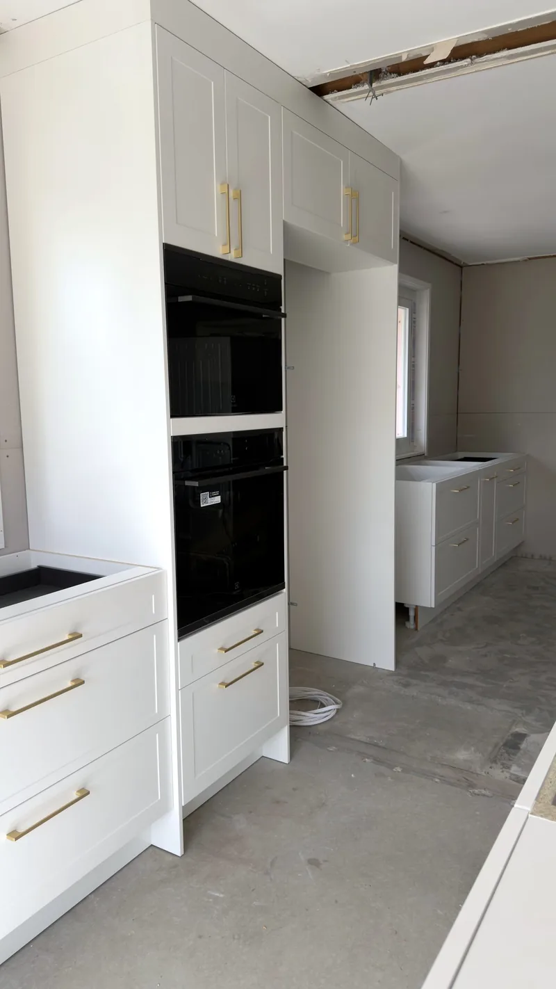 White shaker oven tower with two black wall ovens and brass handles, part way through installation