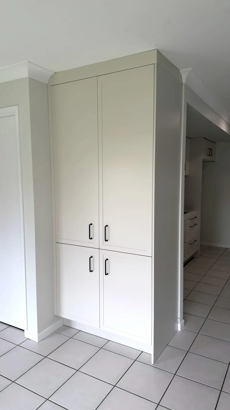 Tall white shaker-style pantry cabinet with black handles