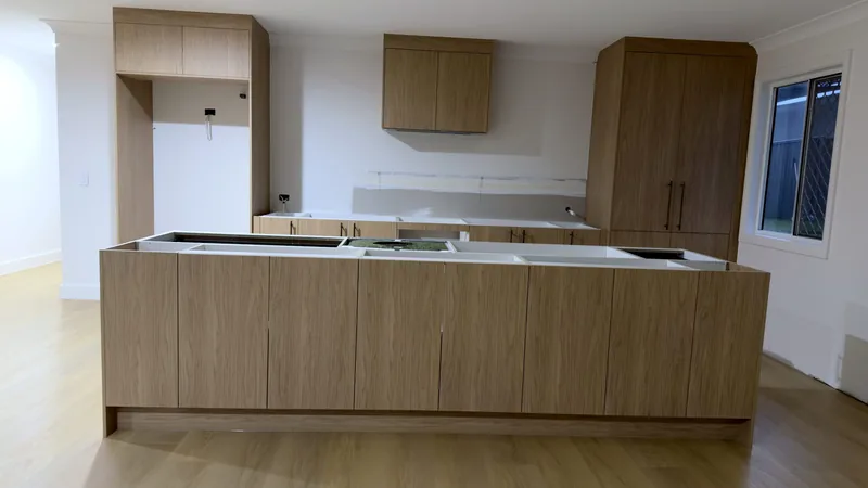 Long oak-look kitchen island in front of a tall pantry unit and an overhead cabinet