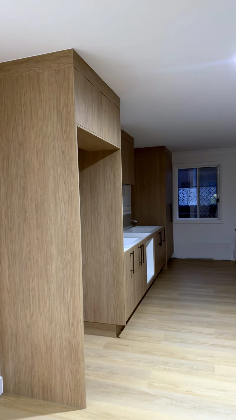 Tall oak fridge surround with an overhead cabinet, leading to an oak galley run