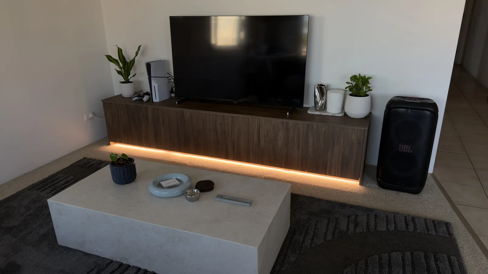 Floating walnut TV unit along a lounge wall with warm LED lighting glowing underneath