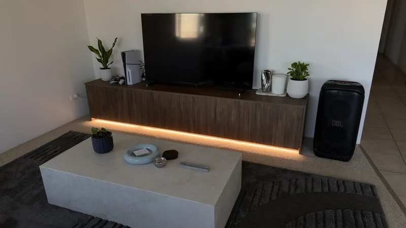 Floating walnut TV unit along a lounge wall with warm LED lighting glowing underneath