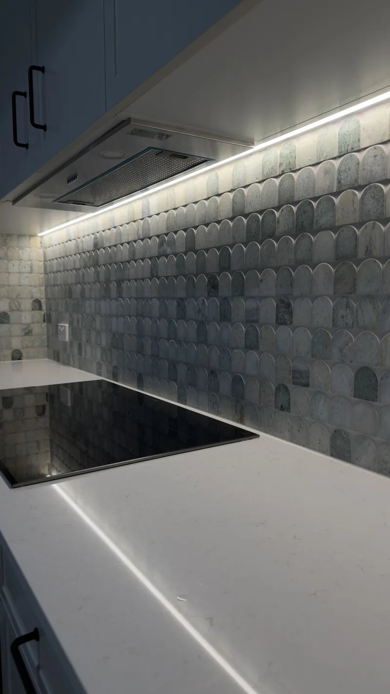 Close view of a white benchtop and black cooktop lit by an LED strip under the overhead cabinets