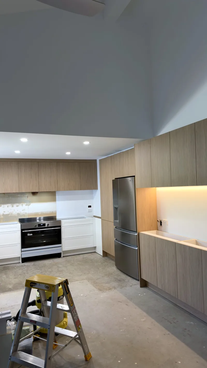 Oak and white kitchen with an oven, fridge space and LED strip lighting, during installation